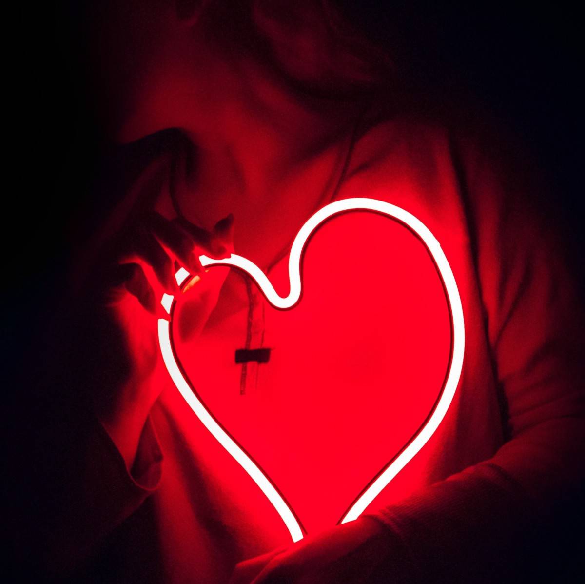 A woman holding a red heart neon sign in the dark, symbolizing customer care.