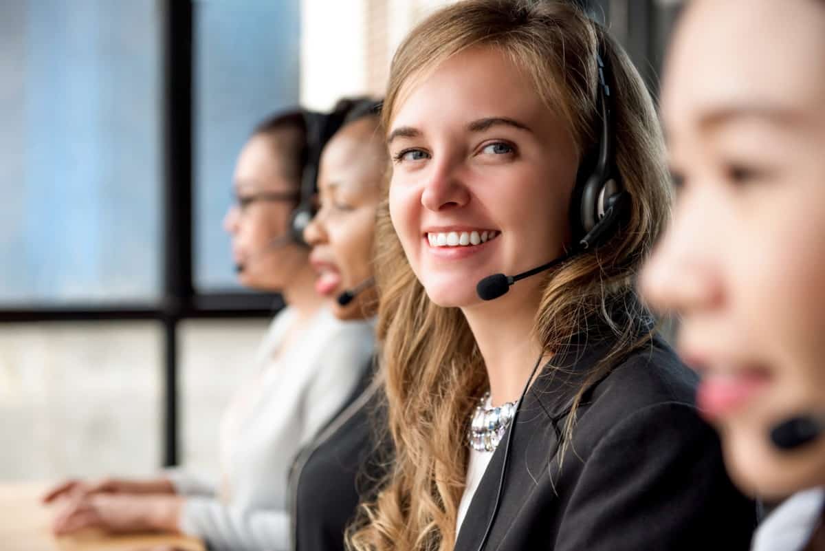 Photo showing call center representatives with headsets at their workstations, with one representative smiling directly at the camera.