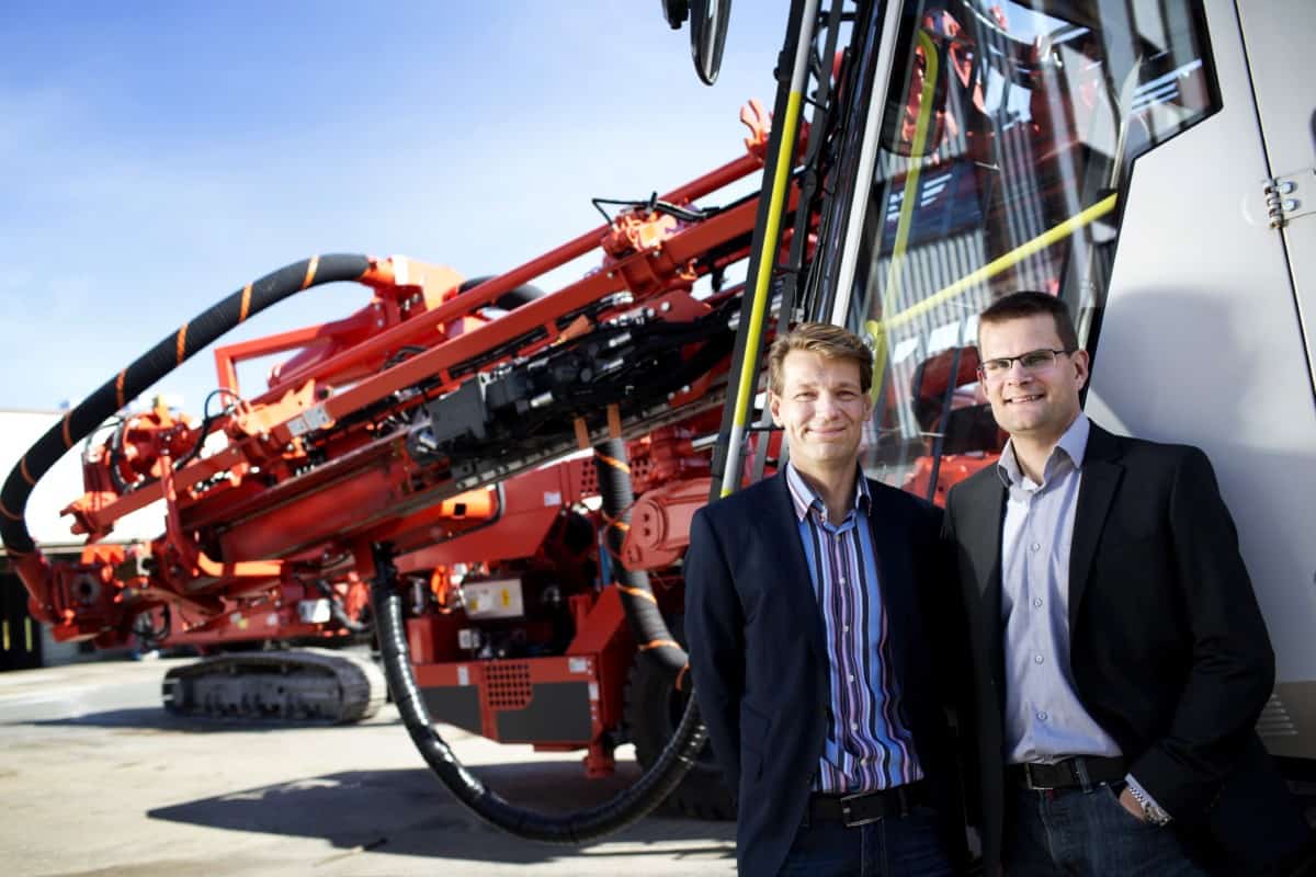 Photo of two smiling Symbio representatives looking at the camera, standing in front of a piece of machinery