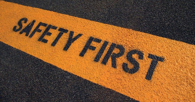 Words 'Safety First' written as a warning in black letters on a yellow strip, prominently displayed on a black tar road.