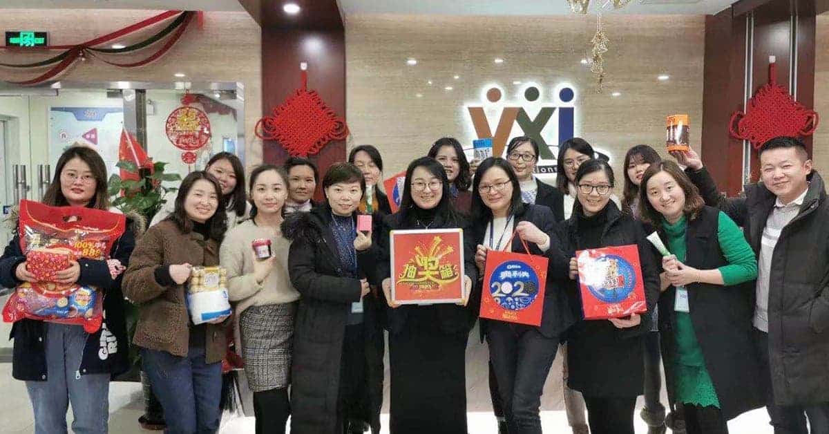 Photo of a group of people standing in a VXI office in China, each holding gifts, posing together with the VXI China logo visible in the background.
