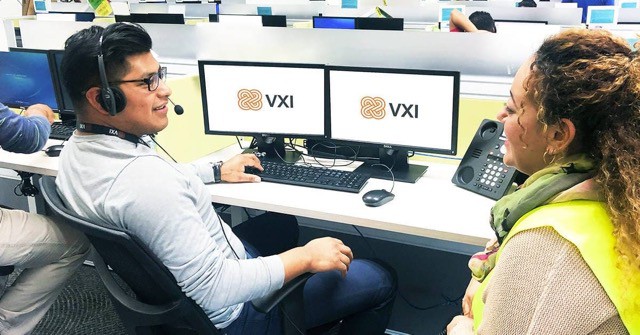 A VXI coach and employee sitting at a desk with dual monitors during a training session