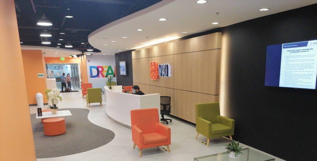 The reception area of a VXI office with colorful chairs and a tv.
