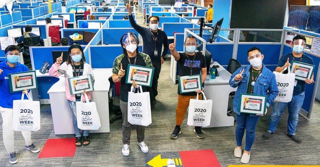 A group of people standing in an office wearing masks and posing with gifts during Customer Service Week.