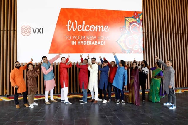 Photo of a group of VXI employees posing in front of a sign in India, celebrating the launch of VXI Global Solutions' entry into the Indian market.